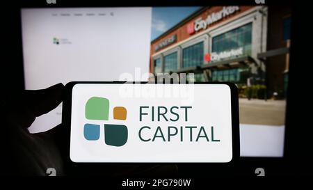 Persona che tiene il telefono mobile con il logo della società immobiliare canadese First Capital REIT sullo schermo di fronte alla pagina web. Messa a fuoco sul display del telefono. Foto Stock