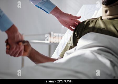 Primo piano del medico che scuote le mani con il paziente e lo sostiene mentre si sdraiava sul letto in ospedale Foto Stock