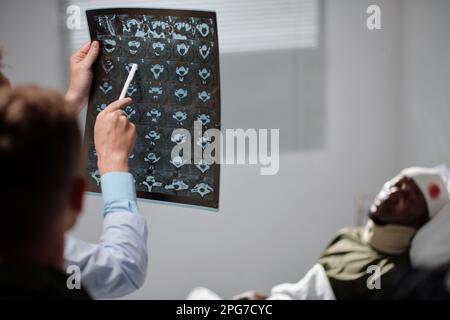 Primo piano del medico che indica l'immagine radiografica del paziente e la esamina, e spiega il problema al visitatore mentre si trovano in reparto Foto Stock