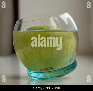 Una mela verde in un bicchiere d'acqua su sfondo chiaro Foto Stock