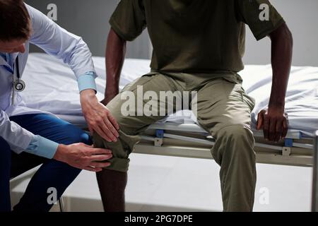 Primo piano del medico che esamina la gamba del soldato in ospedale militare Foto Stock