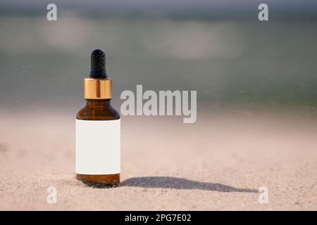 Bottiglia ambrata di olio abbronzante o siero sulla sabbia all'ombra. Etichetta trasparente, mockup Vista frontale dall'altezza degli occhi Foto Stock