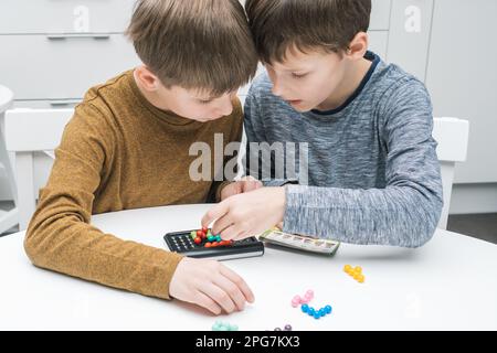 Due ragazzi penitenti ed entusiasti che giocano un gioco da tavolo educativo e strategico con campo nero e palline colorate sul tavolo. Risolvere enigma e trovare Foto Stock