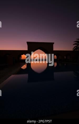 Alba oltre un arco alla fine di una piscina infinity. Presso il Tilal Liwa Hotel deserto resort vicino Abu Dhabi, Emirati Arabi Uniti EMI Foto Stock