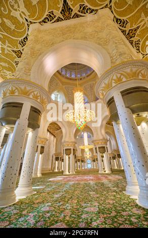 Vista mozzafiato degli interni, finiture d'oro in fantasia nel tappeto, colonne, lampadario. Presso la Grande Moschea dello Sceicco Zayed ad Abu Dhabi, Emirati Arabi Uniti Foto Stock