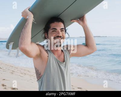 Ritratto di surfista ispanico in piedi sulla spiaggia tenendo la sua tavola da surf Foto Stock