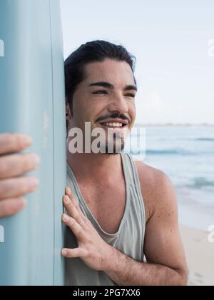 Ritratto di surfista ispanico che tiene la sua tavola da surf sulla spiaggia Foto Stock