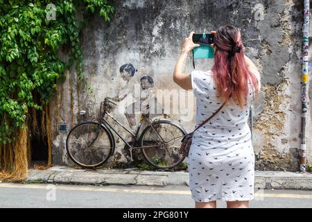 Penang, Malesia - 7 febbraio 2023: Giovane donna prende Una foto di Street Art Boy e ragazza in bicicletta su Un muro a George Town sull'isola di Penang in Mala Foto Stock