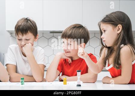 Gioiosa, premurosa bambini, ragazzi e ragazze che giocano a bordo gioco con dadi e limite di tempo, ascoltare le regole. Gioco da tavolo strategico con dadi e figure Foto Stock