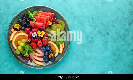Deliziosa insalata sana di frutta fresca, bacche e fiori commestibili sul piatto. Mangiare pulito. Vista dall'alto. Foto Stock