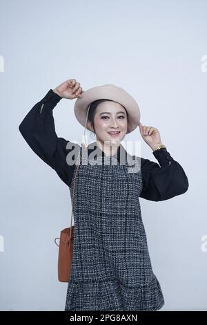 Affascinante ed elegante, questa donna asiatica in un cappello elegante è la quintessenza del cool disinvolto. Il suo sorriso fiducioso e l'eleganza informale la rendono perfetta Foto Stock