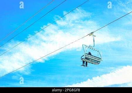 Sciatore in seggiovia contro un cielo blu vibrante. Sport invernali, viaggi e turismo in background. Foto Stock