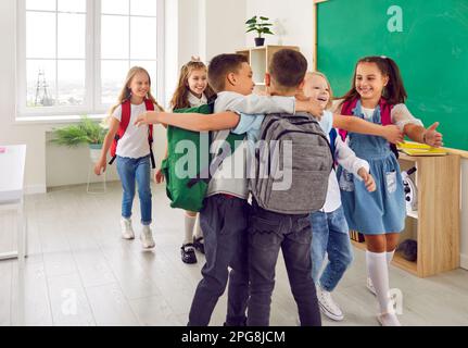 Gruppo di piccoli amici della scuola si abbracciano strettamente come arrivano a scuola prima delle classi. Foto Stock