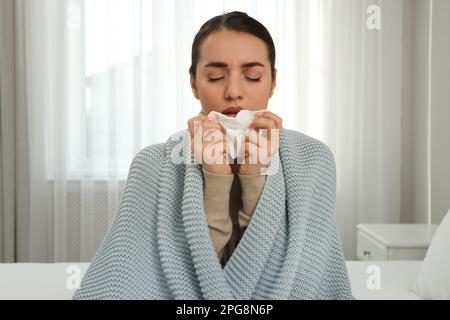 Giovane donna malata con tessuto avvolto in maglia a plaid a casa Foto Stock