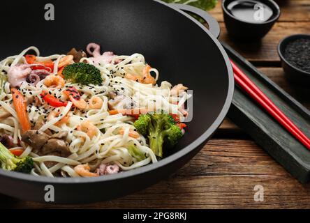 Mescolare le tagliatelle fritte con pesce e verdure in wok su tavolo di legno, primo piano Foto Stock