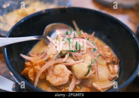 Un recipiente per la cottura a vapore con zuppa di pesce calda e saporita, sormontato da gamberetti piccanti e piccanti, su un tavolo di legno Foto Stock