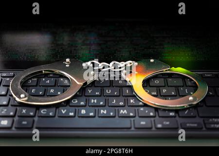 Manette sul primo piano del notebook. Concetto di criminalità informatica. manette metalliche su una tastiera nera. Foto Stock