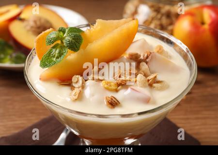 Gustoso yogurt alla pesca con muesli, menta e frutta in ciotola da dessert sul tavolo, primo piano Foto Stock