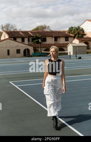 Intera lunghezza di giovane donna in pantaloni cargo bianco a piedi vicino al campo da tennis a Miami, immagine stock Foto Stock