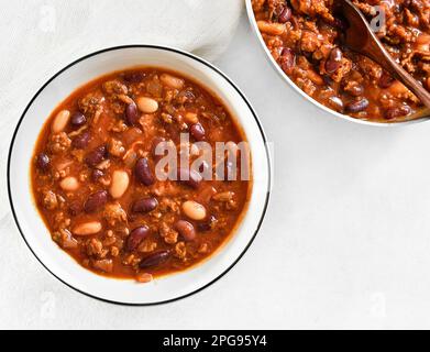 Fagioli stufati con carne macinata, pepe jalapeno e pancetta in ciotola su fondo di pietra bianca. Vista dall'alto, disposizione piatta, primo piano Foto Stock