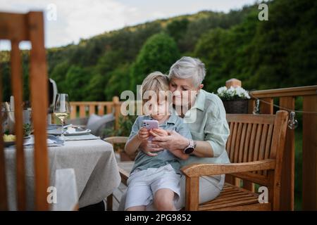 Bambino con la nonna che guarda in smartphone durante la festa barbecue. Foto Stock