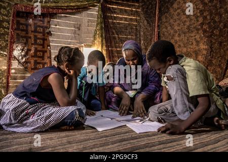 Famiglia della tribù Haratin svantaggiata nella loro capanna nel distretto di Larghiti. I bambini possono frequentare la scuola grazie all'aiuto della Fondazione Sahel, ONG di Brahim Ramdhane, a Nouakshott, in Mauritania. Durante le vacanze, la madre studia con i bambini nella loro capanna. Foto Stock