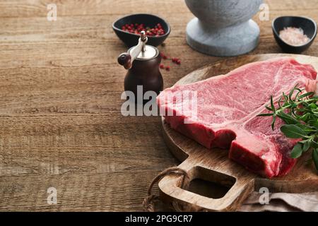 Bistecca con osso a T crudo spesso. Carne di manzo cruda e invecchiata a secco con erbe e sale su fondo scuro. Messa a fuoco selettiva e spazio di copia. Foto Stock