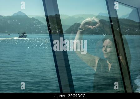 Donna che ha riflettuto nella finestra su una nave passeggeri e che ha fatto una forma di cuore in una giornata estiva soleggiato sul lago di Lucerna con la montagna in Svizzera. Foto Stock