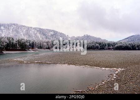 La neve bianca si trova sulla pittoresca spiaggia di pietra vicino alla foresta, vicino alla baia del fiume Katun, sulle montagne Altai in Siberia. Foto Stock