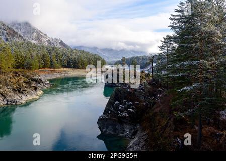 Rive di pietra di origine vulcanica sul fiume d'autunno Katun in montagna con neve e alberi forestali con una spiaggia di sabbia ad Altai. Foto Stock