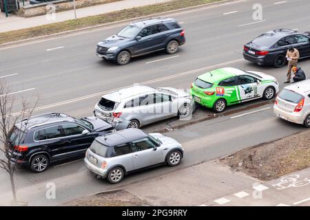 Riga, Lettonia - 15 febbraio 2023: Incidente stradale con tre automobili su una strada cittadina. I conducenti si trovano vicino alle auto distrutte e compilano i documenti per l'assicurazione. Foto Stock