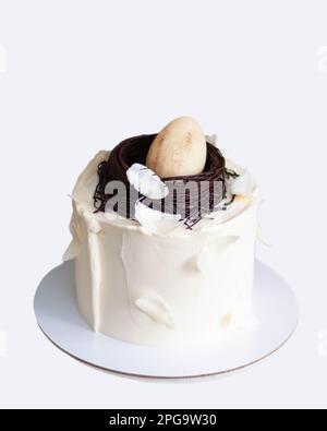 Elegante torta di pasqua decorata con nido di uccello al cioccolato, uova e piume. Sfondo bianco con spazio di copia. Orientamento verticale Foto Stock