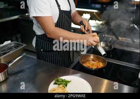 Chef grattugiare il formaggio sulla pasta, vista in primo piano delle mani Foto Stock