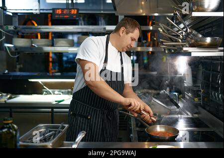 Chef aggiungendo pepe alla salsa con pomodoro per la pasta Foto Stock