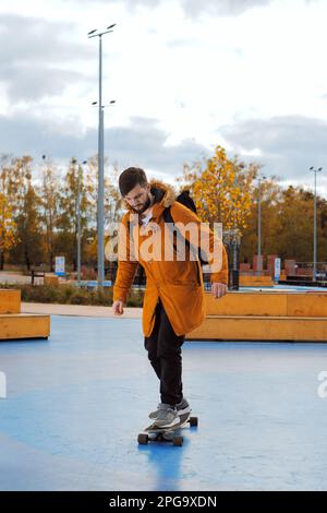 Un giovane adulto elegante e casual a tutta altezza in skateboard in movimento presso lo skatepark, vista laterale Foto Stock