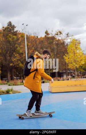 Un giovane adulto elegante e casual a tutta altezza in skateboard in movimento presso lo skatepark, vista laterale Foto Stock