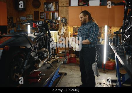 Brutale biker strofinando le mani durante la riparazione del motore di motocicletta Foto Stock