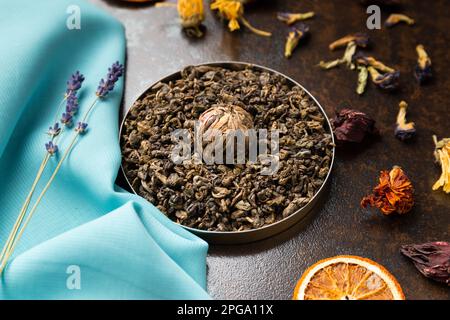 Composizione di fettine verdi, di tè e di arancia secca su fondo blu e marrone. Tè a foglie grandi, fiori secchi e patatine di agrumi Foto Stock