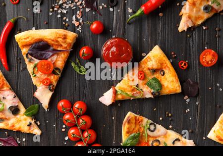 Fette di pizza a jerky, olive, formaggio ed erbe sono disposti su uno sfondo di legno scuro, un ramo di pomodori ciliegini freschi, salse Foto Stock