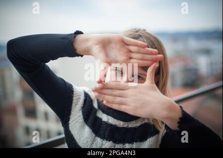 Cattura i momenti più belli. Giovane donna in un maglione a righe in bianco e nero crea una cornice con le mani, la città sullo sfondo. Foto Stock