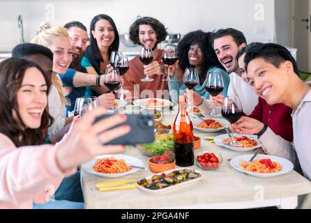 un gruppo di amici multietnici prende un selfie smartphone mentre mangia pasta e brinda con il vino Foto Stock