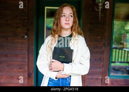 Una giovane donna con un'espressione seria sta fuori, tenendo la Sacra Bibbia Foto Stock