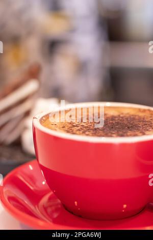 Cioccolata calda servita in tazza rossa con torta sullo sfondo Foto Stock