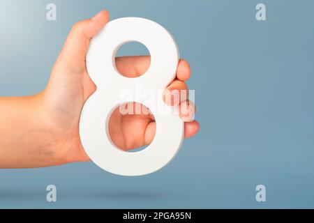 Otto in mano. Una mano tiene un numero bianco 8 su uno sfondo blu. Concetto con il numero otto. Compleanno 8 anni, percentuale, ottavo grado o giorno Foto Stock