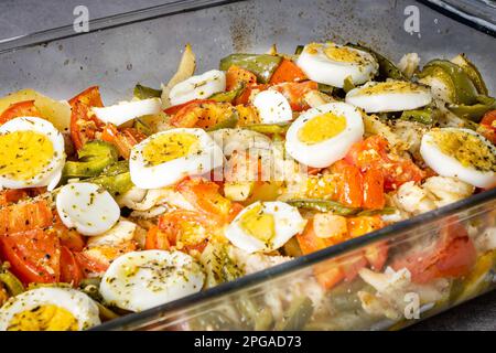 Gomes de sa baccalà arrosto in olio d'oliva con pomodori, peperoni, cipolle, uova sode e origano. In una teglia rettangolare di vetro. Vi. Perpendicolare Foto Stock