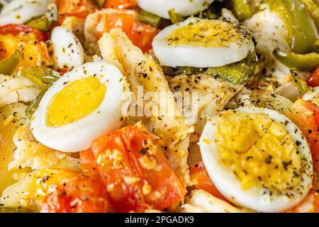 Gomes de sa baccalà arrosto in olio d'oliva con pomodori, peperoni, cipolle, uova sode e origano. In una teglia rettangolare di vetro. Vista di dettaglio. Foto Stock