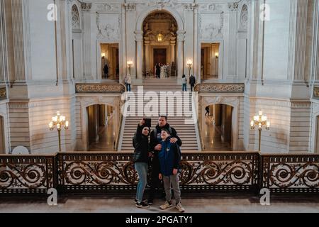 Le persone scattano foto davanti alla grande scalinata all'interno del Municipio, che è stato splendidamente restaurato e riportato alle sue condizioni originali. La scala presenta ringhiere ornate, intarsi intricati e uno stupefacente lampadario sospeso dal soffitto. Dopo due anni di lavori di ristrutturazione, l'iconico municipio di San Francisco ha finalmente riaperto le sue porte al pubblico dal giugno 2021. Il progetto da $550 milioni di dollari mirava a ripristinare gli elementi storici dell'edificio e a modernizzarlo per soddisfare le esigenze del 21st° secolo. Il progetto ha comportato il restauro della cupola iconica del Municipio, che oggi vanta un edificio di Foto Stock