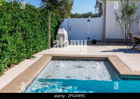La vasca idromassaggio concia parte di bordo di una nuova piscina con bordi di cemento abbronzato nel cortile recintato di una nuova casa di costruzione Foto Stock