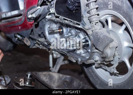 Il meccanico della motocicletta controlla le condizioni del sistema di trasmissione automatica o del sistema della frizione dello scooter in officina. Concetto di riparazione e manutenzione della motocicletta Foto Stock