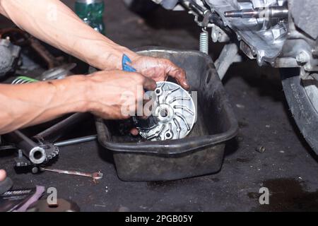 Il meccanico della motocicletta controlla le condizioni del sistema di trasmissione automatica o del sistema della frizione dello scooter in officina. Concetto di riparazione e manutenzione della motocicletta Foto Stock